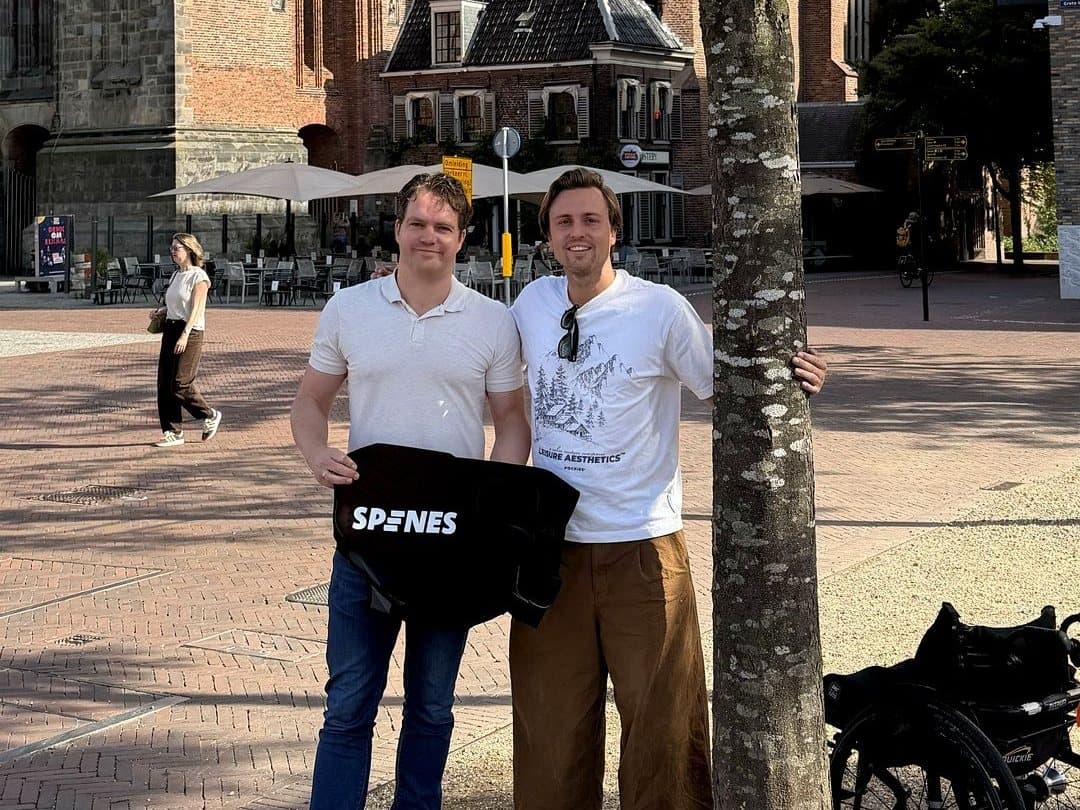 Strategie.nl en Spines op een zonnig plein voor een kerk, met een Spines-rugbeschermer in de hand